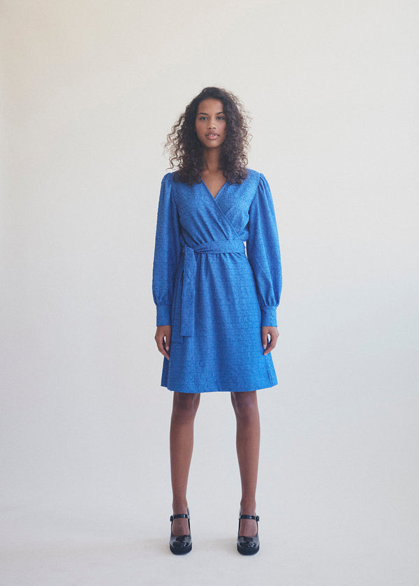 Short dress with wrap detail, tiebelt at the waist, and v-neckline. TalissaMD wrap dress has long puffsleeves with cuff. Designed in a structured material.