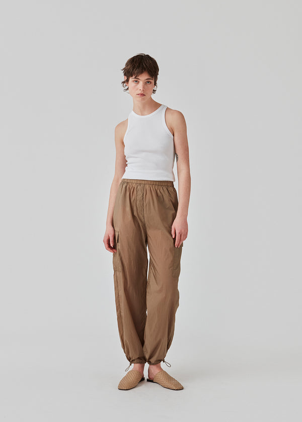 Pants in recycled nylon in the color Dune. AmayaMD pants have a high waist and straight legs with adjustable drawstring at hem. Covered elasticated waist and two large pockets on the legs.