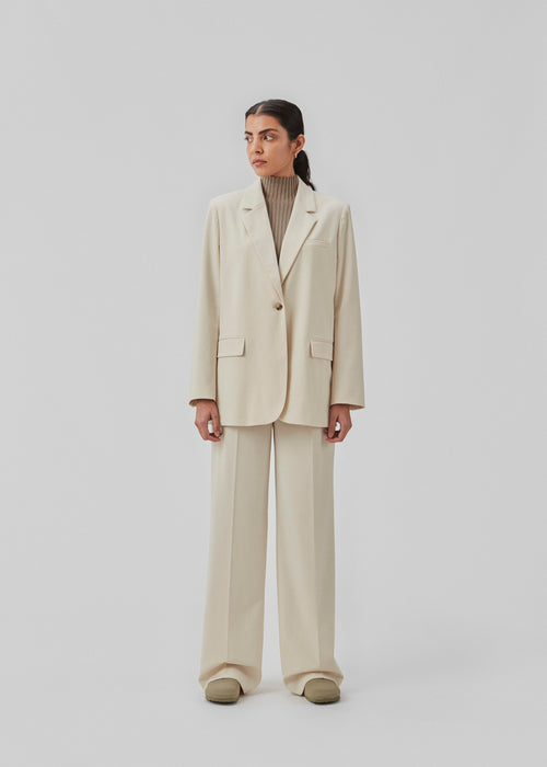 Pants in beige with wide legs and a medium waist. AnkerMD pants have creases, button and zip fly, side pockets, and paspel back pockets. The model is 177 cm and wears a size S/36.  Shop matching blazer: AnkerMD blazer.