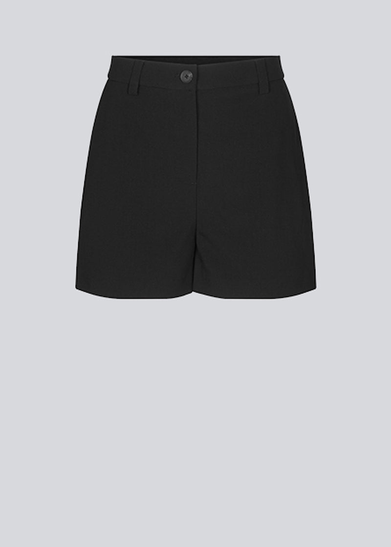 Wide-legged shorts in black with a medium waist. AnkerMD shorts have creases down the front, zip fly and buttons, side pockets, and fake back pockets. The model is 174 cm and wears a size S/36.