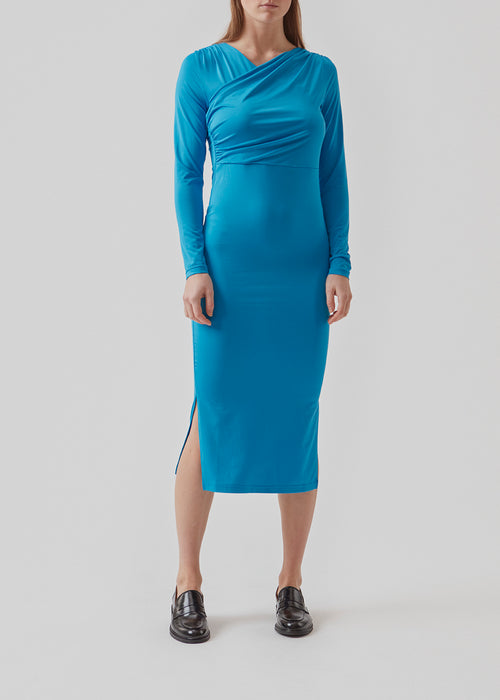 Form-fitted dress in blue with long skirt with slits at both sides. ArniMD dress has a high v-neckline med flattering wrap detail over the chest.