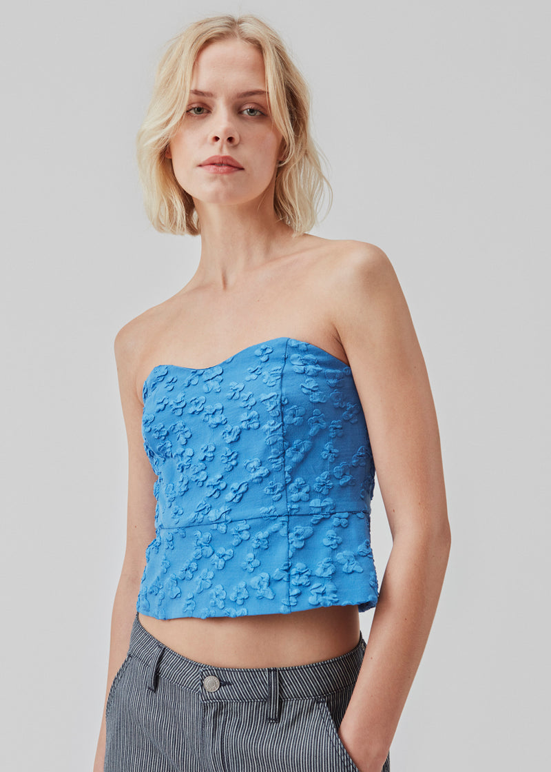 Crop top in blue without sleeves with a heart-shaped neckline and a slight peplum-effect. AtiraMD crop top has a structured floral pattern.  The model is 177 cm and wears a size S/36.