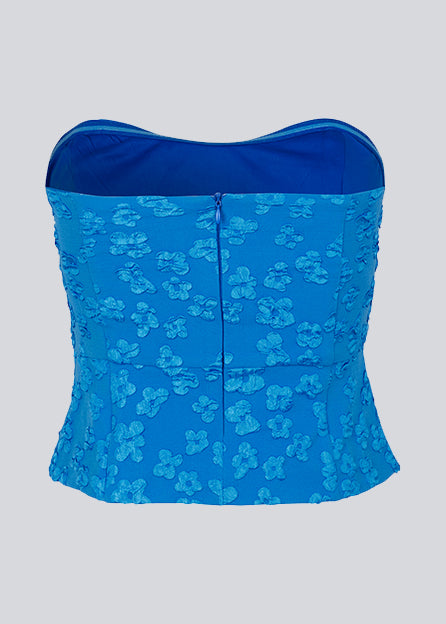 Crop top in blue without sleeves with a heart-shaped neckline and a slight peplum-effect. AtiraMD crop top has a structured floral pattern.  The model is 177 cm and wears a size S/36.