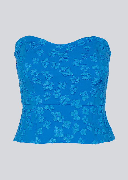 Crop top in blue without sleeves with a heart-shaped neckline and a slight peplum-effect. AtiraMD crop top has a structured floral pattern.  The model is 177 cm and wears a size S/36.