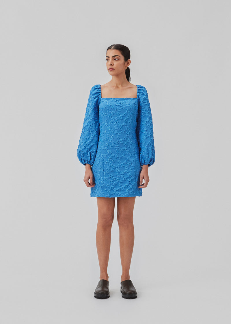 Short dress in blue with all-over floral structure. AtiraMD dress has long balloon sleeves and a more fitted body. The neckline is square in front and back.  The model is 177 cm and wears a size S/36.
