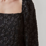 Short dress in black with all-over floral structure. AtiraMD dress has long balloon sleeves and a more fitted body. The neckline is square in front and back.