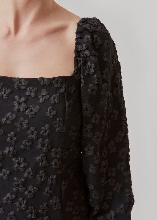 Short dress in black with all-over floral structure. AtiraMD dress has long balloon sleeves and a more fitted body. The neckline is square in front and back.