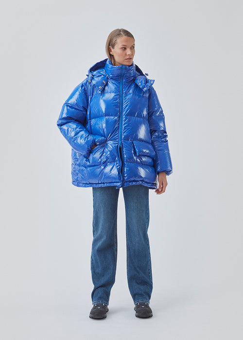 BanaMD Jacket in blue is a puffer in a shiny material with natural down filling. The jacket has two padded pockets in front and with a removable hood.