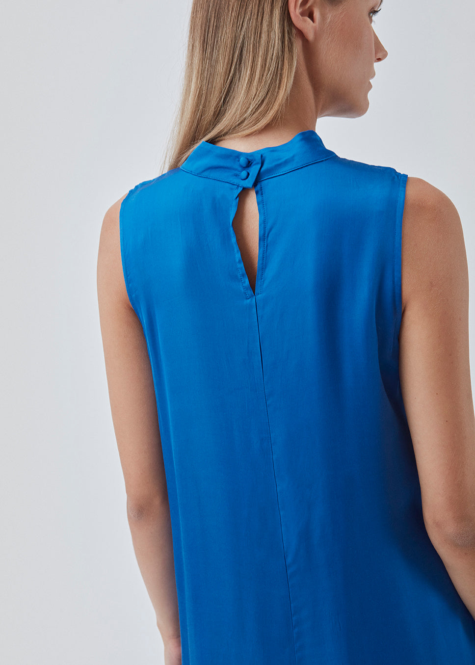 Long dress with a high neck in a softly draping more responsible satin quality. BeateMD dress is sleevesless and with a small opening in the neck with a discreet button closure.