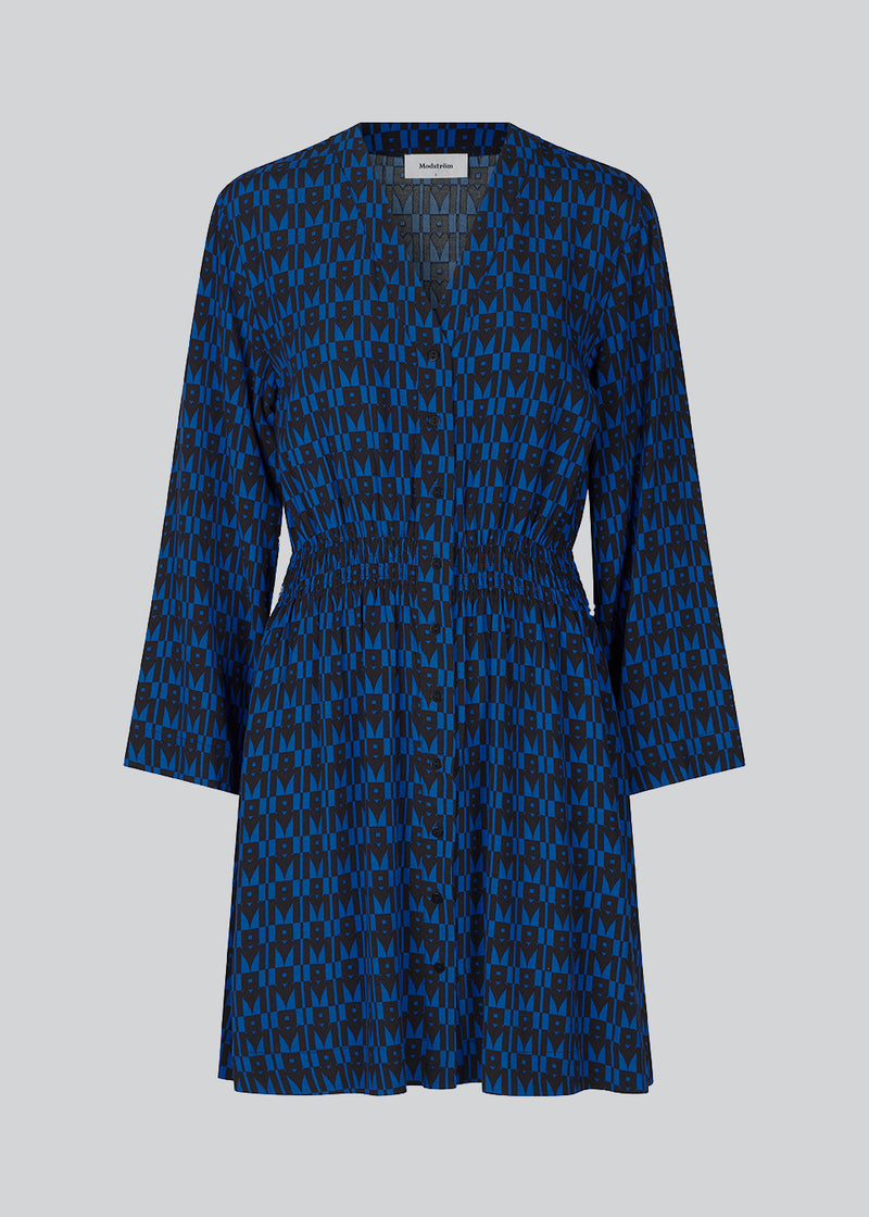 Short printed dress in the color: Graphic Heart Bright Ocean. BorysMD print dress has a v neckline med button closure in the front and smock detail in the waist. The style has long wide sleeves.