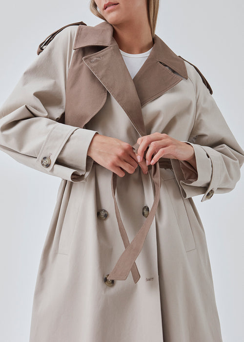 Double-breasted trench coat in woven, cotton quality with contrasting colors. BrodaMD coat has a collar, gun flap, a loose yoke in the side with a tie at the waist. The shape is casual.
