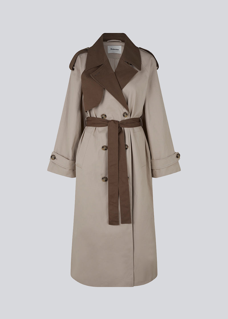 Double-breasted trench coat in woven, cotton quality with contrasting colors. BrodaMD coat has a collar, gun flap, a loose yoke in the side with a tie at the waist. The shape is casual.