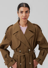 Double breasted dark green trench coat made from a woven cotton. BrodaMD solid coat features a collar, storm flap, and a tie-belt at the waist. The fit is relaxed.