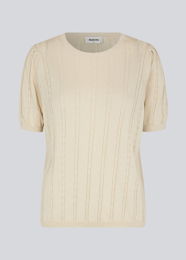 Short sleeved jumper in beige in cable knit with a round neck and puff sleeves. CarltonMD o-neck has a slim and stretchy shape. Shop the matching skirt: CarltonMD skirt. The model is 177 cm and wears a size S/36.