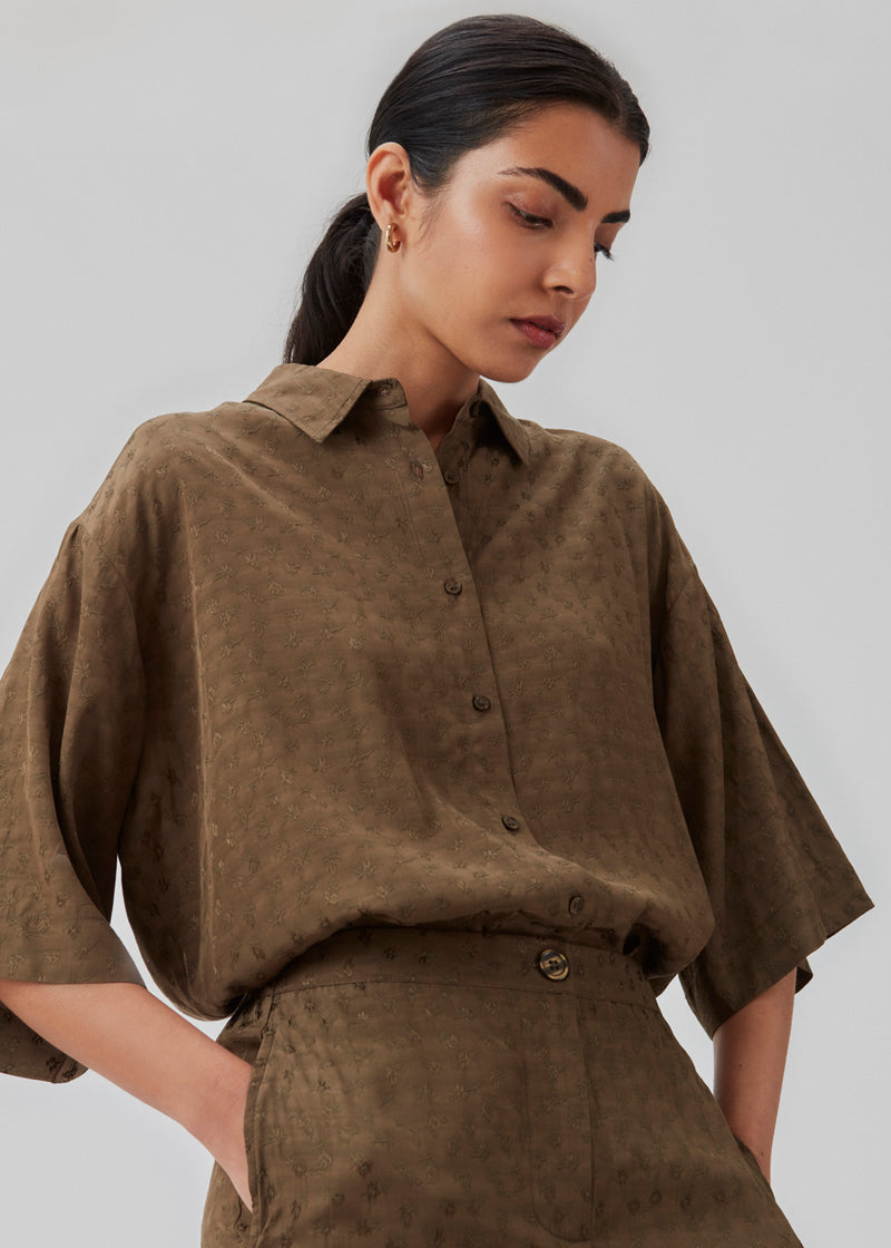 Short-sleeved shirt in the color Dark Forest satin fabric with a pattern. CarmelMD shirt has a loose fit, collar, buttons in front, and long sleeves. The model is 177 cm and wears a size S/36.  Shop matchende busker i samme farve: CarmelMD pants