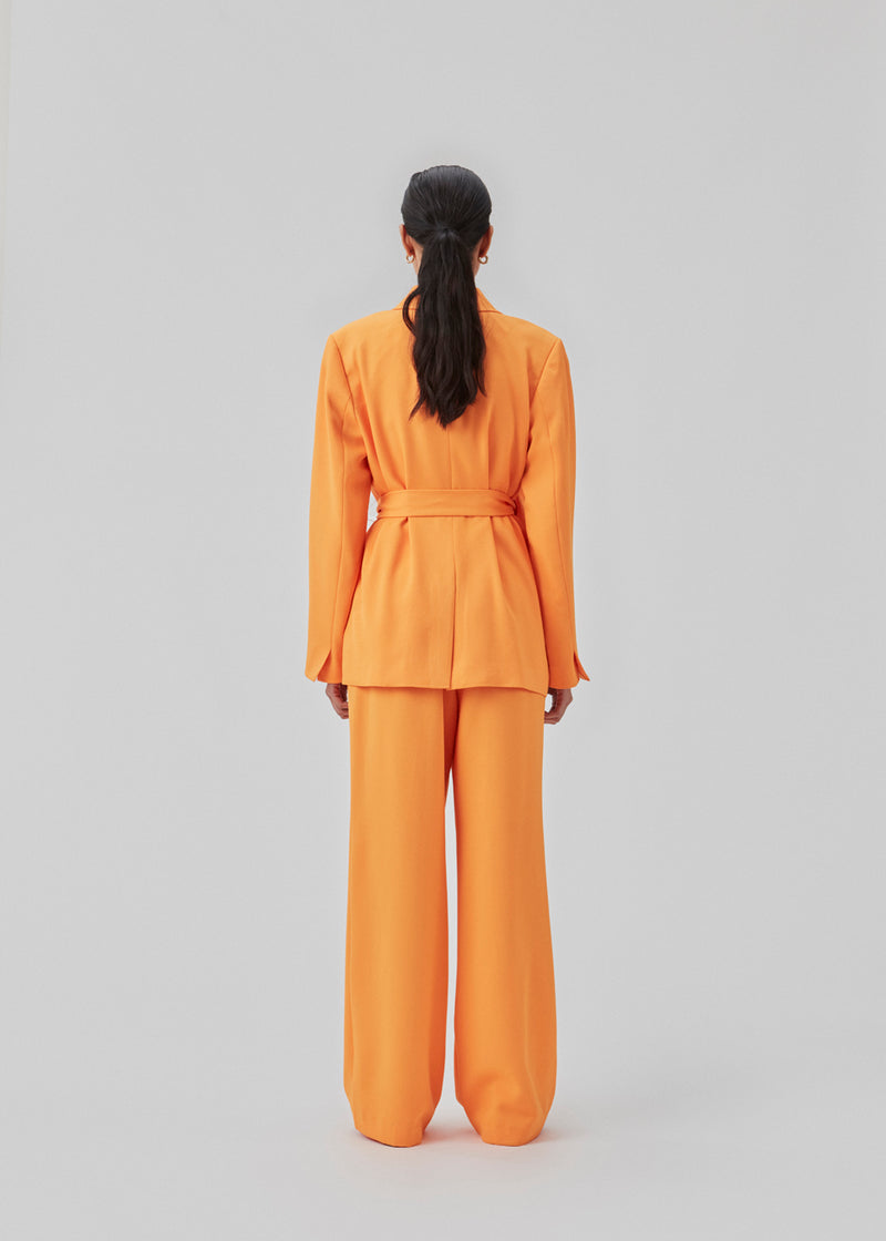 Loose pants in orange with wide legs made from recycled materials. Double pleating in front, zip fly and button closure. The model is 177 cm and wears a size S/36.  Style with the matching blazer: CayaMD blazer