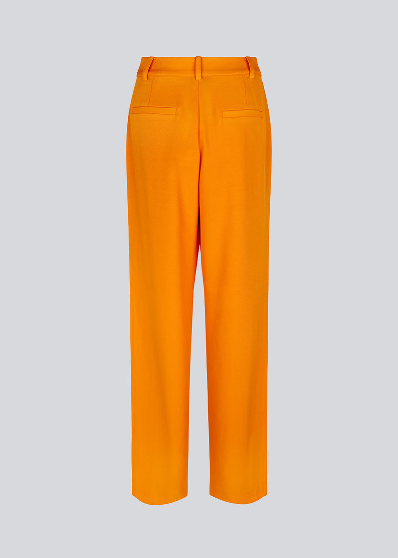 Loose pants in orange with wide legs made from recycled materials. Double pleating in front, zip fly and button closure. The model is 177 cm and wears a size S/36.  Style with the matching blazer: CayaMD blazer