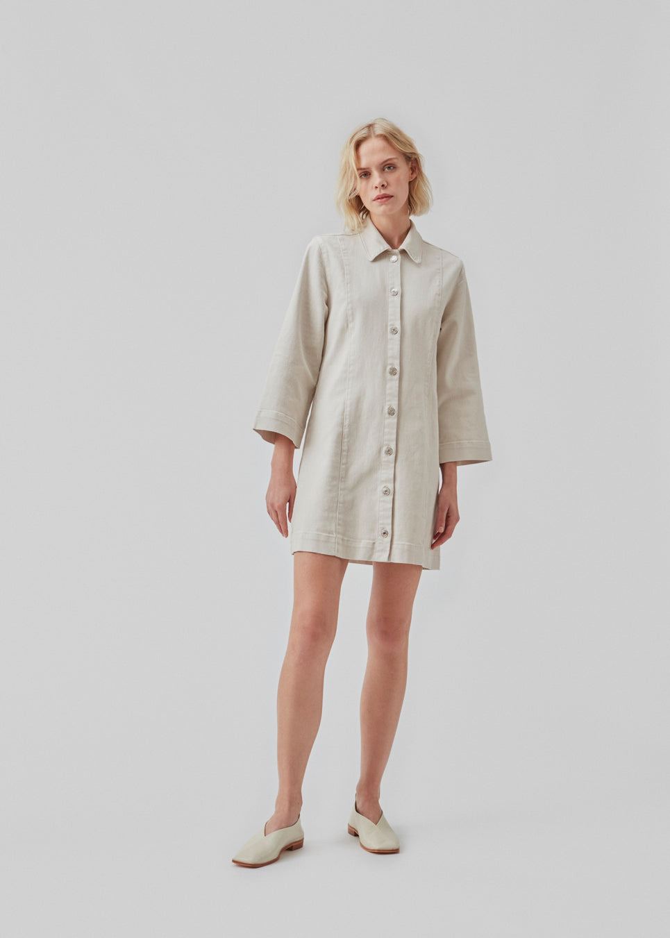 Short denim dress with a slight figure-hugging silhouette. ChikoMD dress has a collar and buttons down the front and 3/4 length wide sleeves. The model is 177 cm and wears a size S/36.  