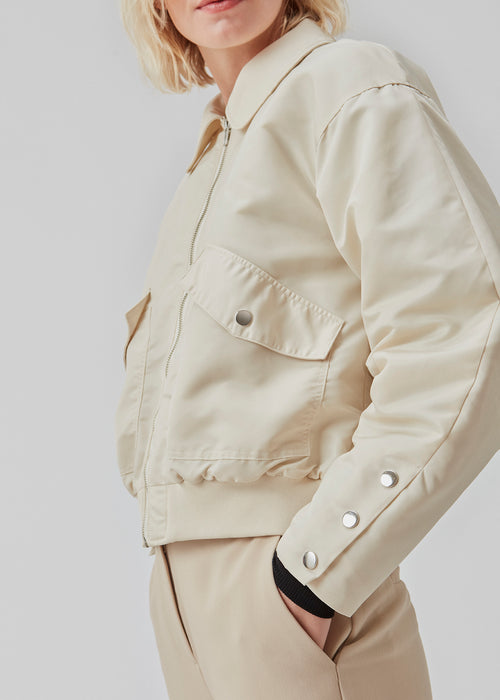 Short, padded bomber jacket in beige. ColtonMD jacket is designed with a collar, zipper in front, and pockets with push buttons. Ribbing at the hem.