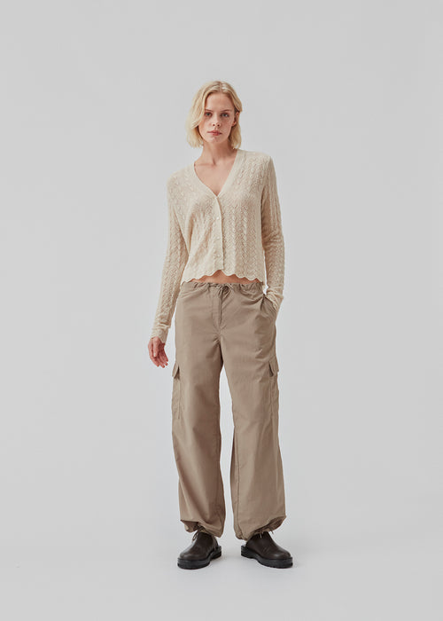 Delicate cardigan in summer sand in wool mix designed with a short length, long sleeves, and a v-neck. CordellMD cardigan has a pattern with holes and a wavy hem.