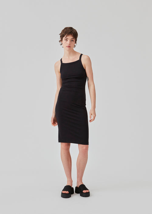 Tight fitted basic black dress in organic cotton jersey. DaeMD dress is sleeveless with a high and straight neckline. The dress cuts below the knees. The model is 177 cm and wears a size S/36.