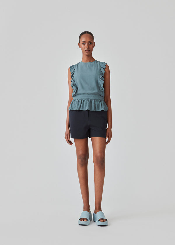 Sleeveless top in the color Stormy Sea with a high neck and a slight peplum effect. DafneMD print top has ruffled details over the shoulders and at the bottom, along with an opening in the back with ties. The model is 177 cm and wears a size S/36.