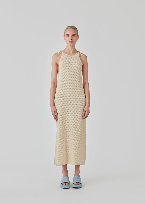 Open knit dress in beige in organic cotton. DariaMD dress has a slim fit with a long skirt, and straps that ties over the shoulder. The model is 177 cm and wears a size S/36.