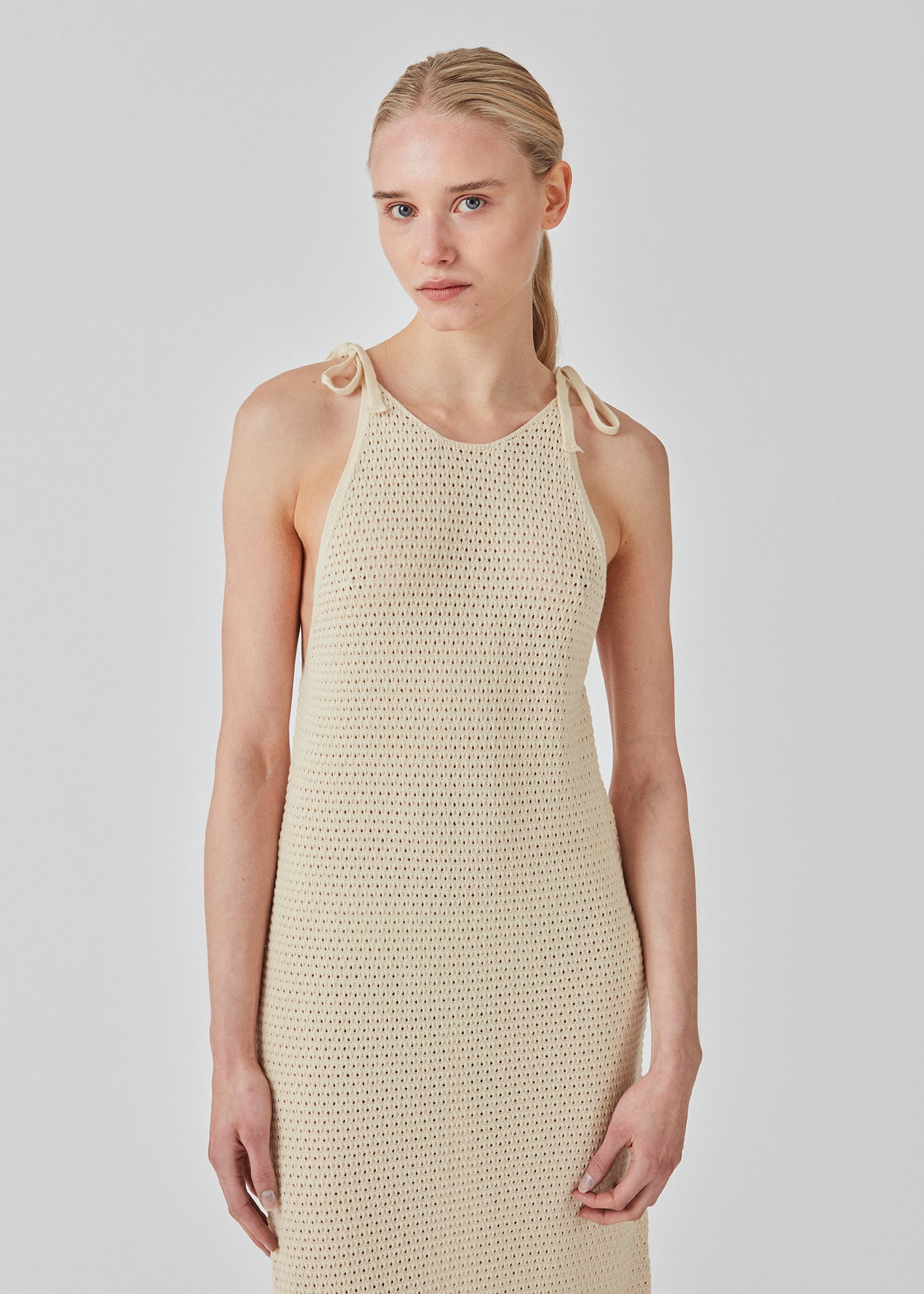 Open knit dress in beige in organic cotton. DariaMD dress has a slim fit with a long skirt, and straps that ties over the shoulder. The model is 177 cm and wears a size S/36.