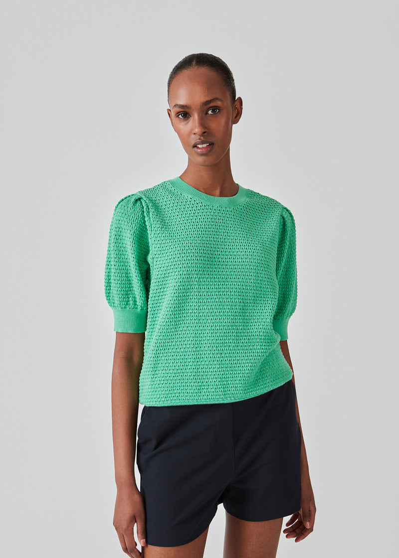 DariaMD o-neck is an open-knitted jumper in green with short puff sleeves and a round neck. Ribbed trimmings at the bottom, neckline, and cuffs. The model is 177 cm and wears a size S/36.