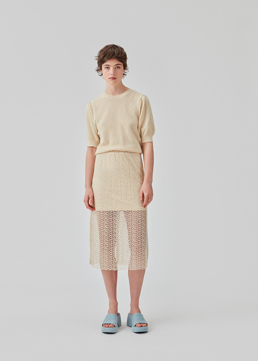 DariaMD o-neck is an open-knitted jumper in beige with short puff sleeves and a round neck. Ribbed trimmings at the bottom, neckline, and cuffs. The model is 177 cm and wears a size S/36.