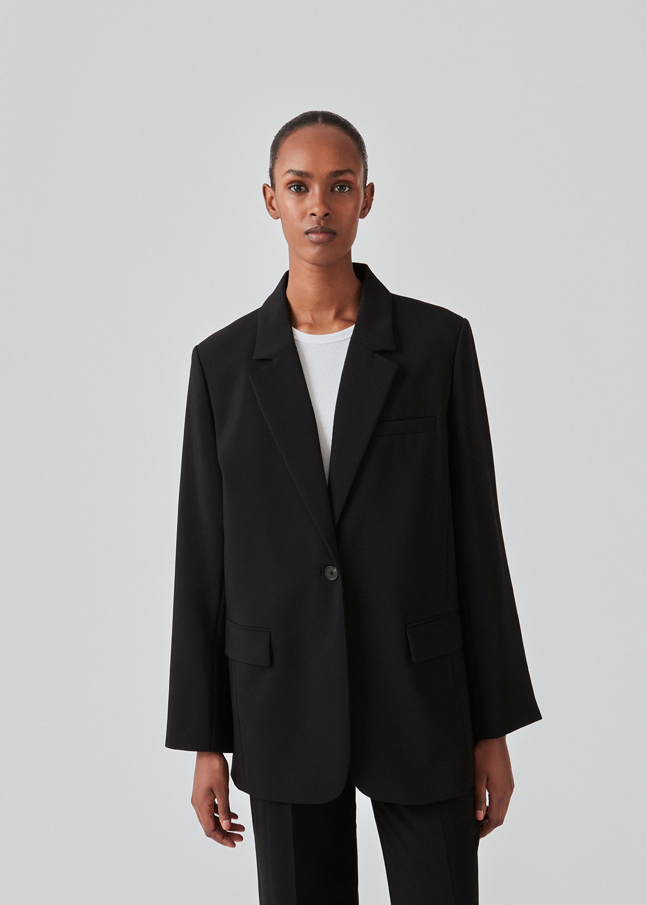 Gale blazer in Black has a classic and elegant design, fulfilled by the beautiful revers collar and a long fit. The blazer has a button closure at the front and a chest pocket at the left side. Buy Gale Pants, Gale straight pants, GaleMD skirt or GaleMD shorts in the same color that fits the Blazer.  The model is 177 cm and wears a size S/36.  This blazer has a spacious fit. We recommend sizing down.