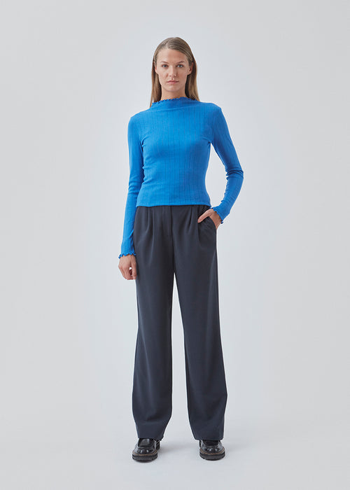 Tight fitted t-shirt in blue with a medium high neck. Issy t-neck has feminine lettuce hem on neck and sleeves. The quality is a soft jersey with a feminine pointelle patter
