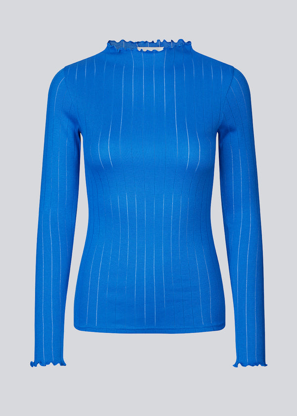 Tight fitted t-shirt in blue with a medium high neck. Issy t-neck has feminine lettuce hem on neck and sleeves. The quality is a soft jersey with a feminine pointelle pattern.