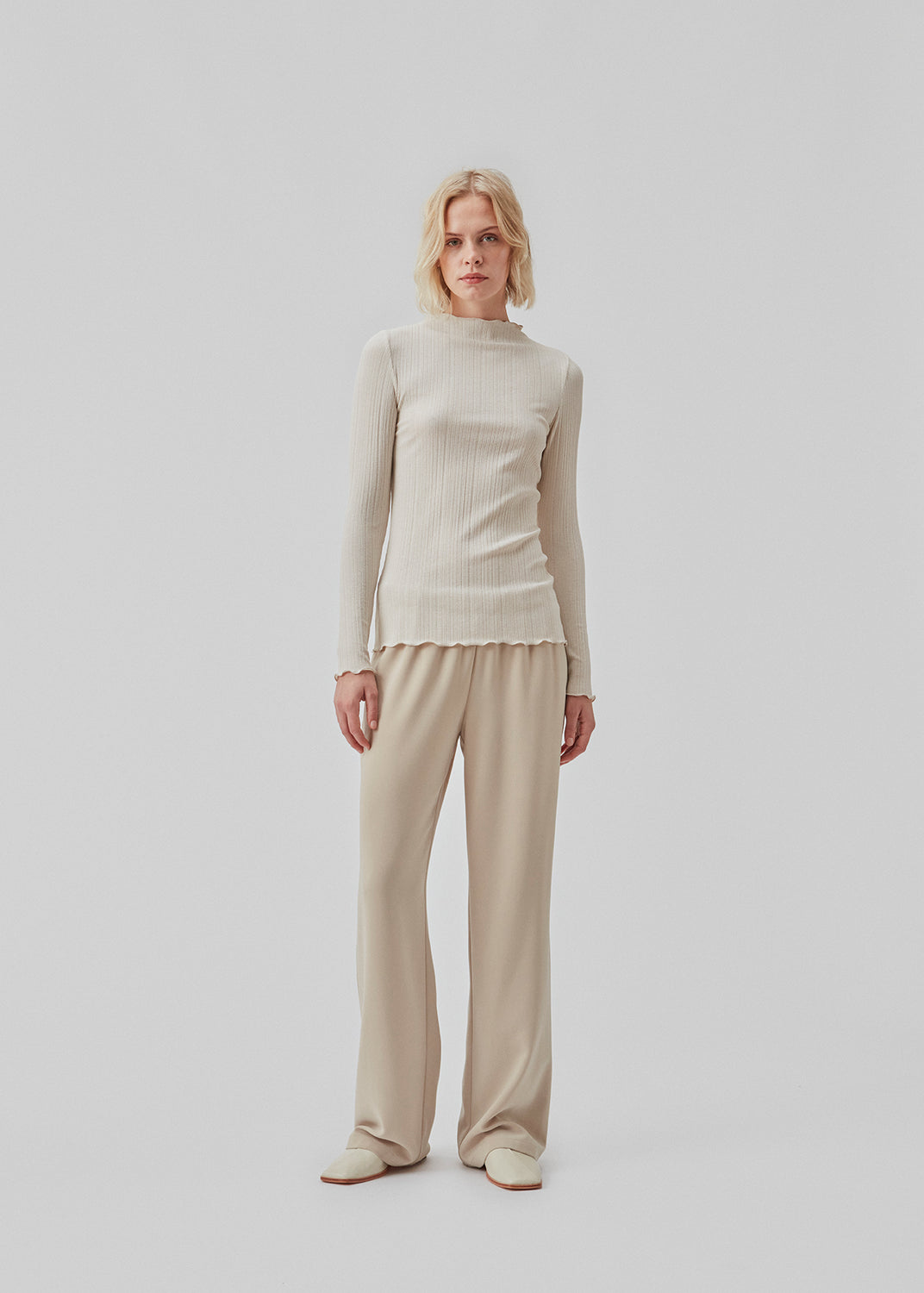 Tight-fitted, beige long sleeved t-shirt with ruffled trimmings on sleeves, at the neck and bottom. Oasis t-neck fits perfectly as a basic style in the wardrobe.   The model is 177 cm and wears a size S/36.
