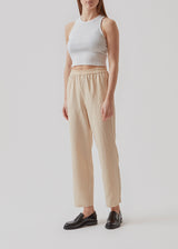 Straight, wide pants in beige in check with elasticated waist, pockets at side, and a decorative fake back pocket. The length is slightly cropped. The model is 173 cm and wears a size S/36.