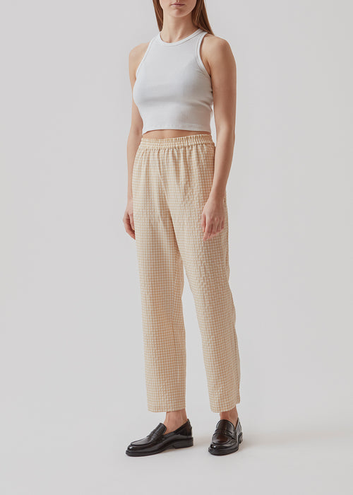 Straight, wide pants in beige in check with elasticated waist, pockets at side, and a decorative fake back pocket. The length is slightly cropped. The model is 173 cm and wears a size S/36.