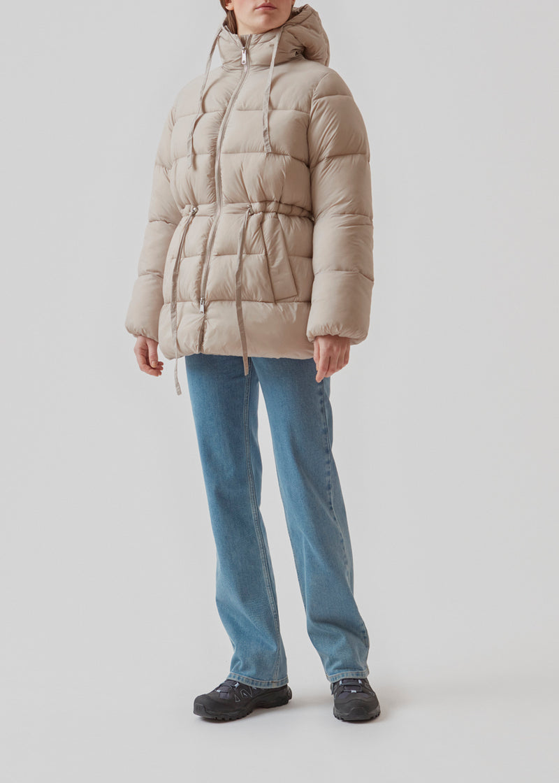 Puffer jacket in beige with an oversized silhouette and adjustable drawstring waist. StellaMD jacket is designed with a high-standing collar, hood, two-way zipper and paspel pockets.