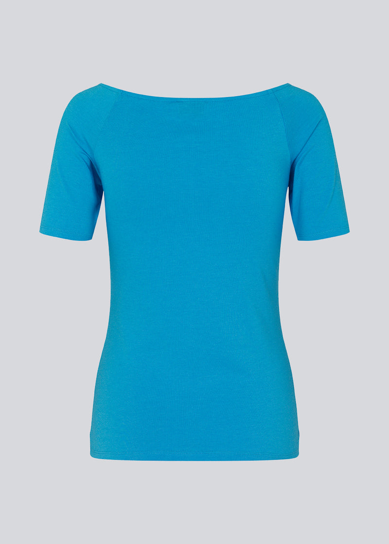 Tansy top in blue has a simple look with a wide neckline at the front and back and narrow sleeves. The top is slim fit without being tight. The model is 174 cm and wears a size S/36
