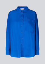 Airy shirt in blue in organic cotton poplin. TapirMD shirt has a collar and buttons in front, with an open chest pocket. Dropped shoulders and long sleeves with cuff and button. Embroidered logo in front.
