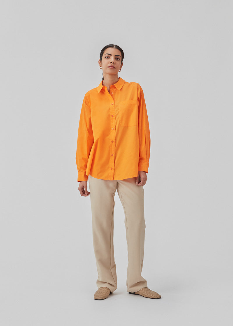 Airy orange shirt in organic cotton poplin. TapirMD shirt has a collar and buttons in front, with an open chest pocket. Dropped shoulders and long sleeves with cuff and button. Embroidered logo in front.  The model is 177 cm and wears a size S/36.