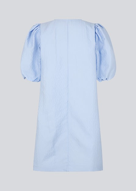 Short dress in a structured and shiny quality in blue. TelmaMD dress has a relaxed fit with a v-shaped neckline and short puff sleeves.